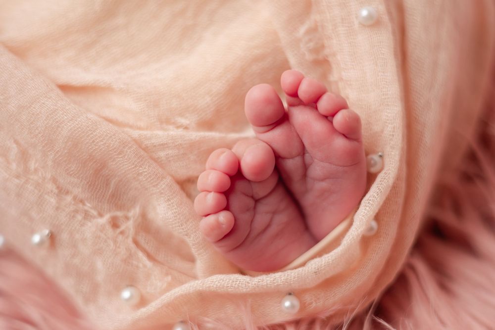 Close-up of tiny newborn baby feet wrapped in soft peach fabric with pearl accents.
