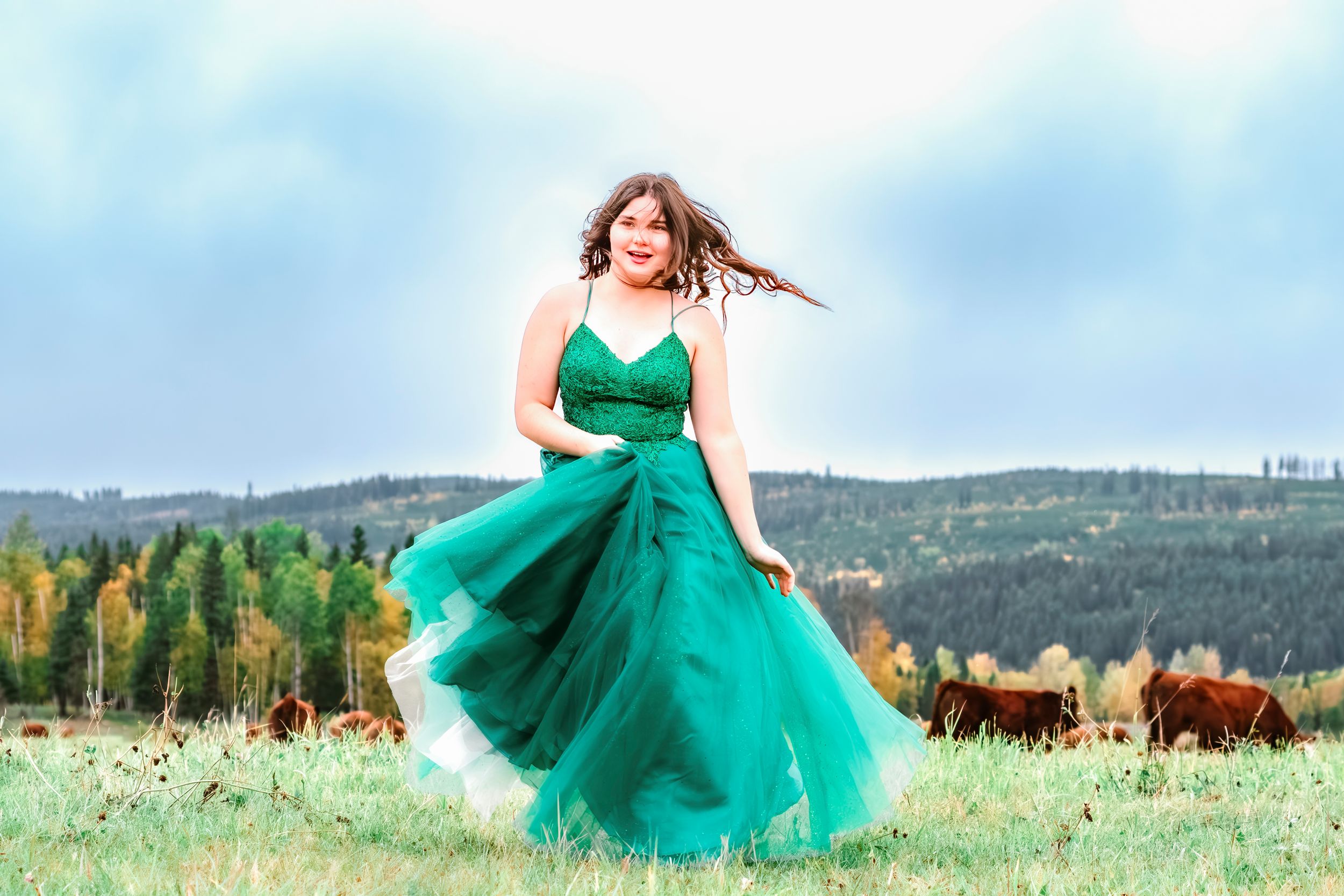 A person in a flowing emerald green dress twirls gracefully in a mountain meadow filled with wildflowers.