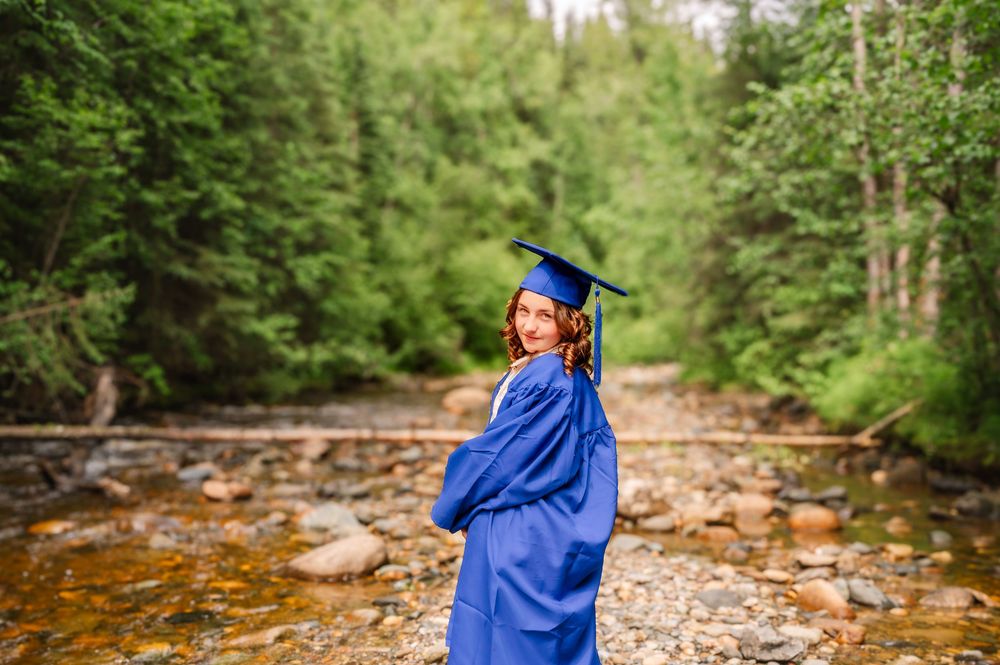 A person in bright blue rain gear walks along a rocky stream bed surrounded by lush forest scenery.