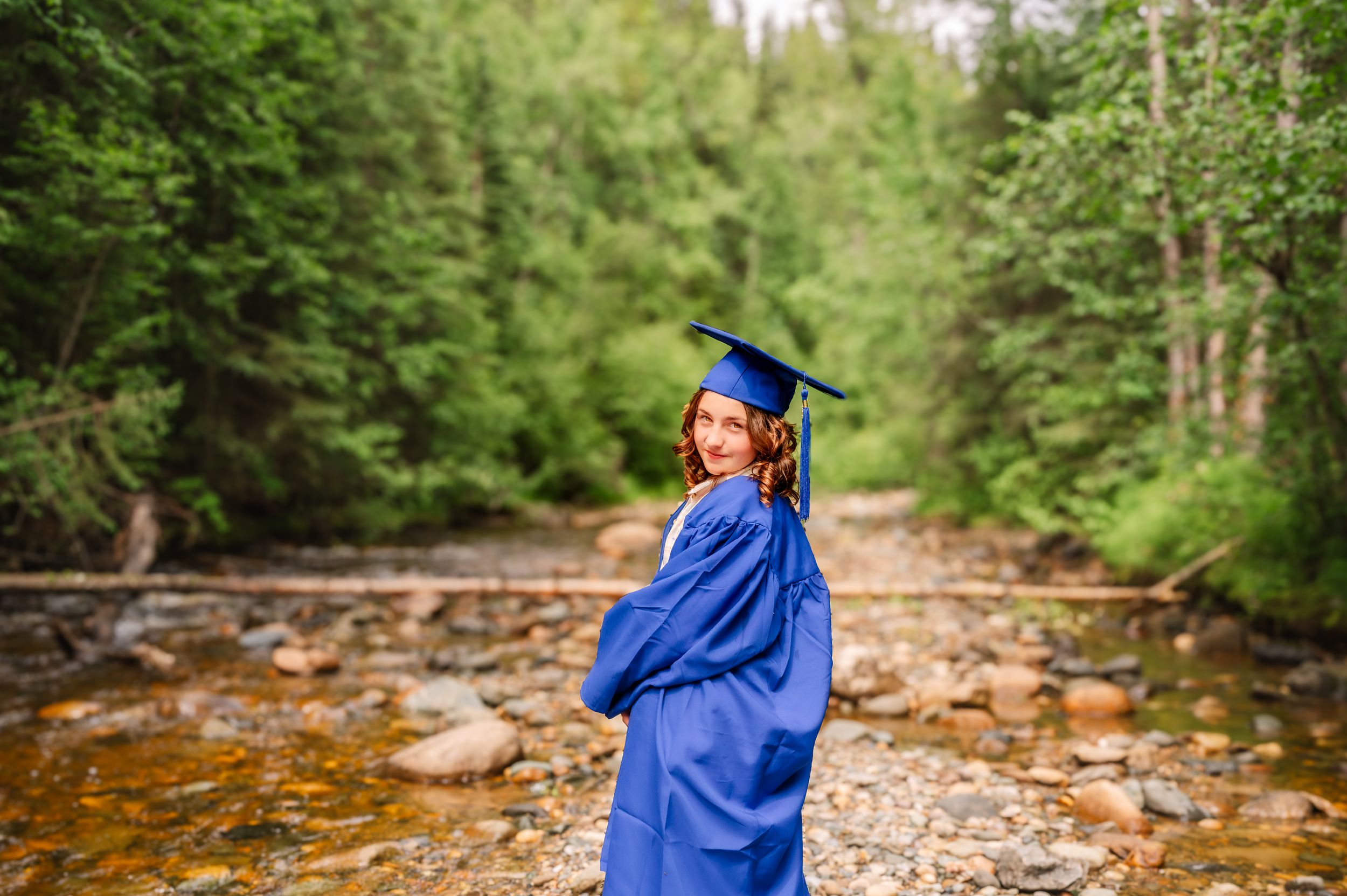 A person in bright blue rain gear walks along a rocky stream bed surrounded by lush forest scenery.