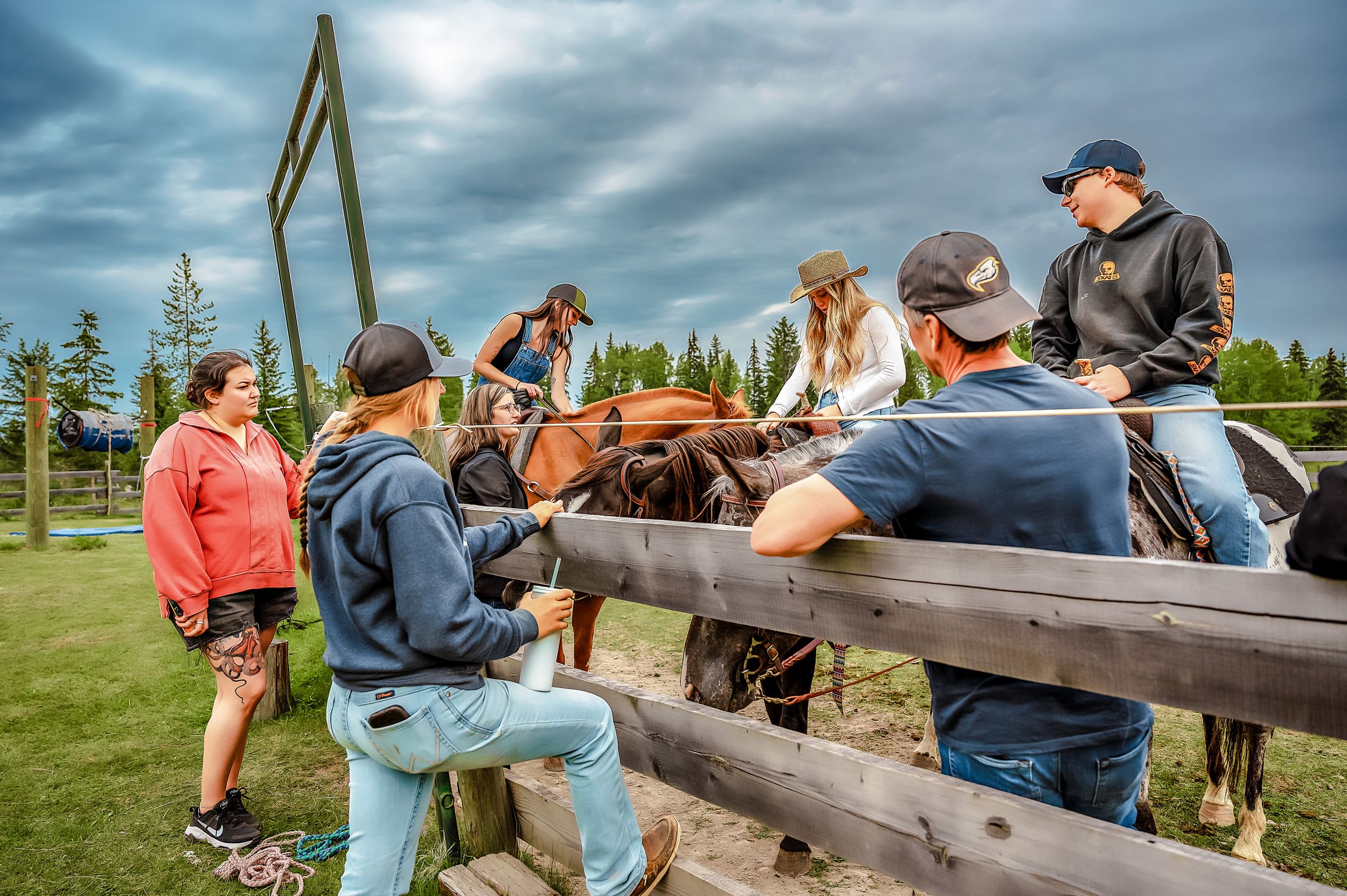 People gather around a wooden fence at a rural outdoor event under dramatic cloudy skies.
