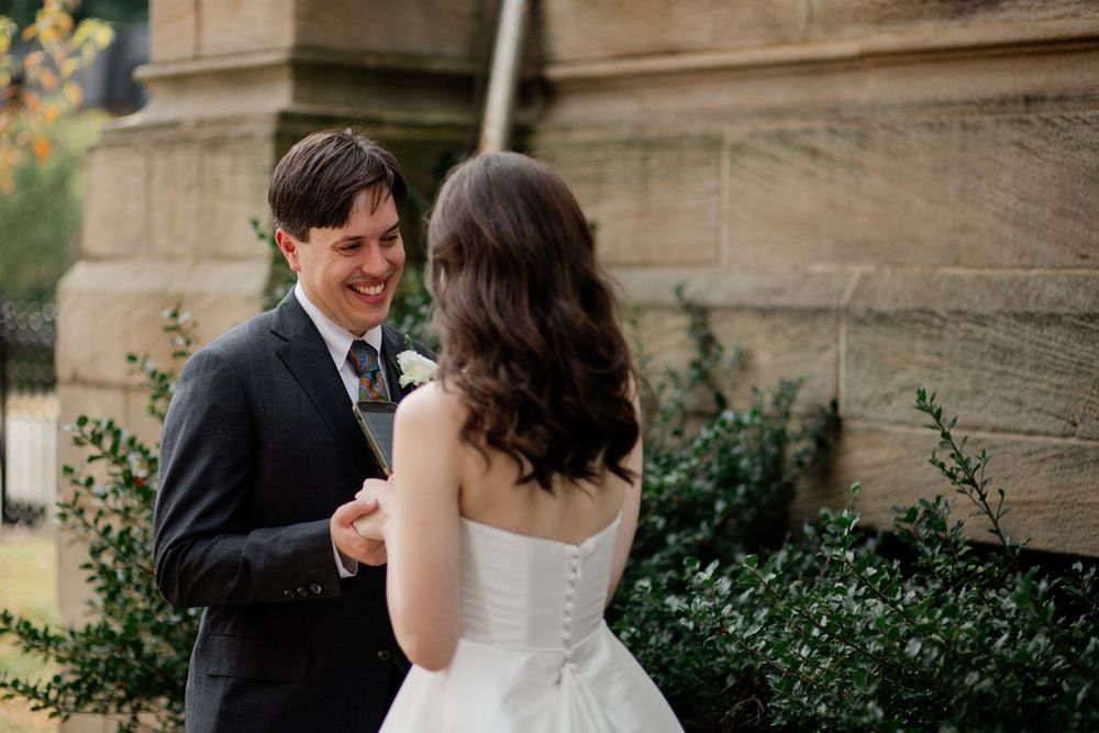 A couple shares an intimate moment during their wedding photoshoot in front of a stone building with ivy.