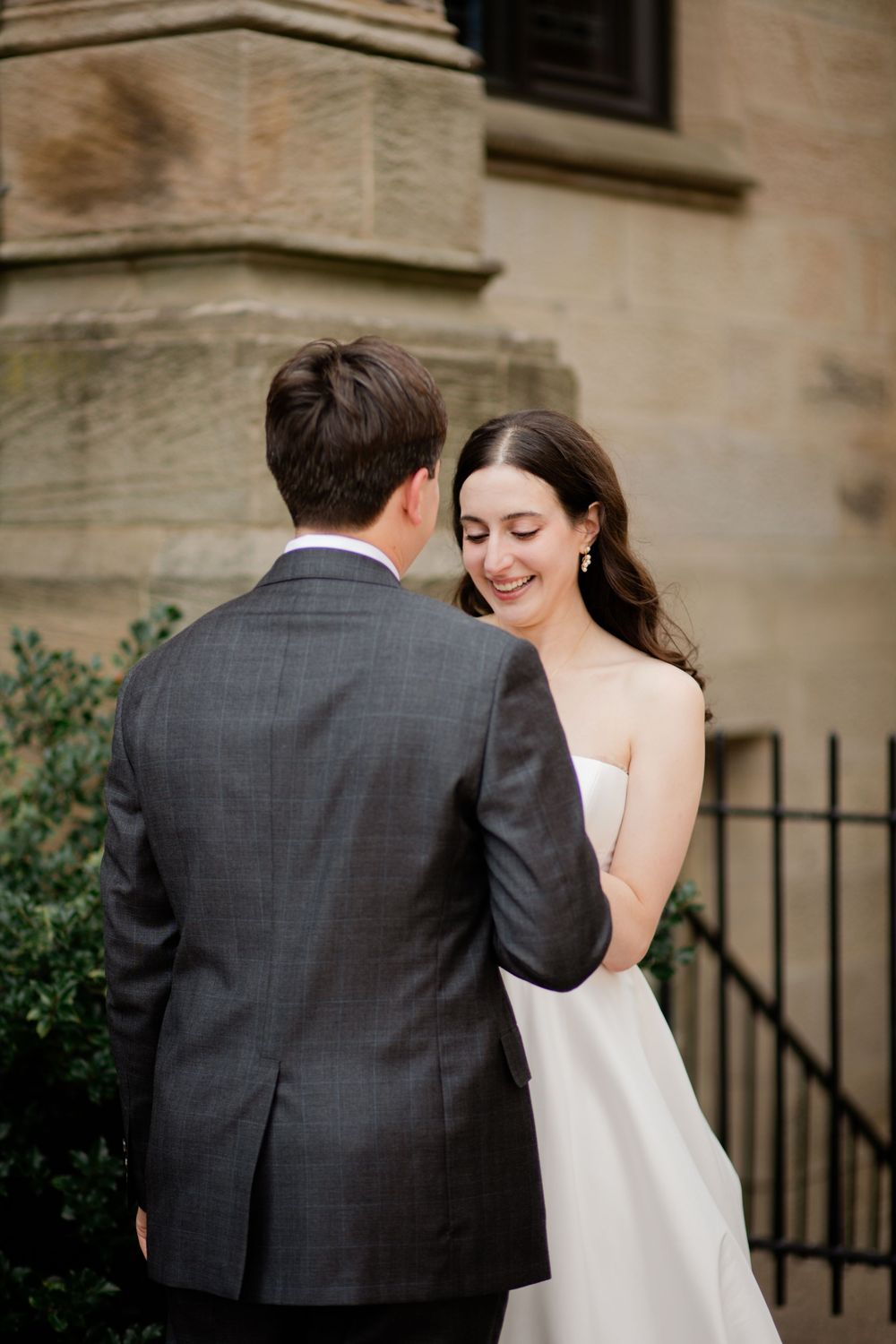 A couple shares a romantic moment in formal wedding attire outside a stone building with elegant architecture.
