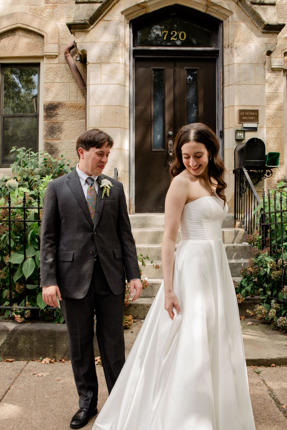 A wedding couple shares candid moments in front of a historic stone building entrance with climbing vines.