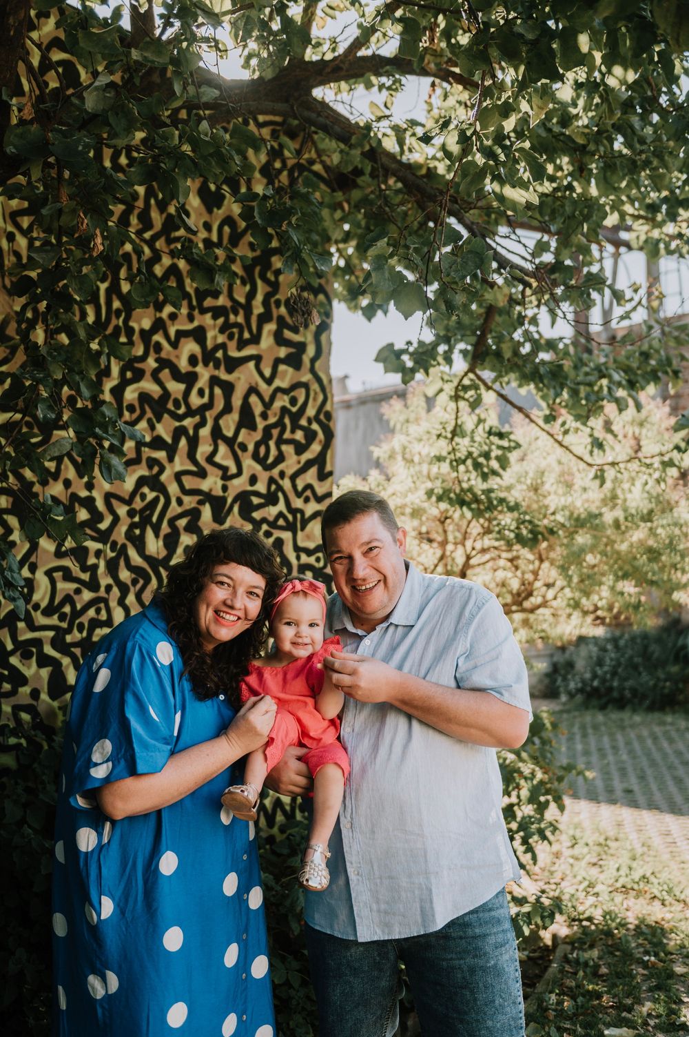Parents holding their cute little daughter dressed in pink in front of a colorful graffiti wall in Johannesburg