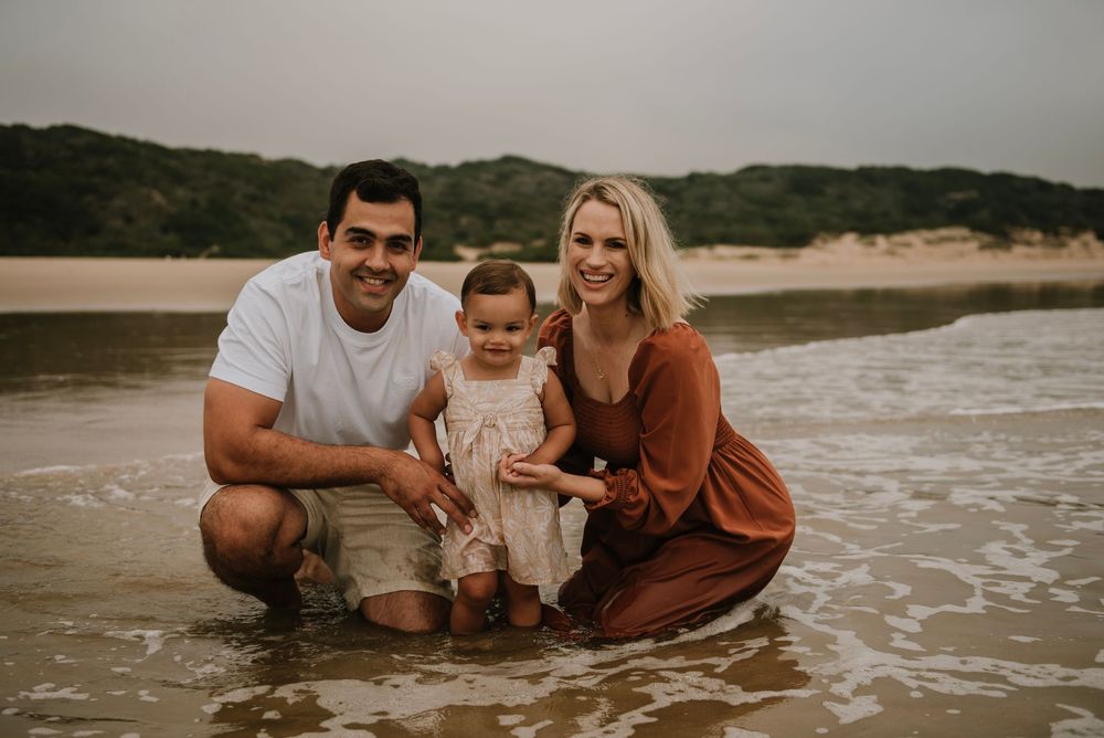Parents holding their daughter on Hartenbos Beach as waves crash in behind them, capturing a joyful and dynamic family moment by the sea.