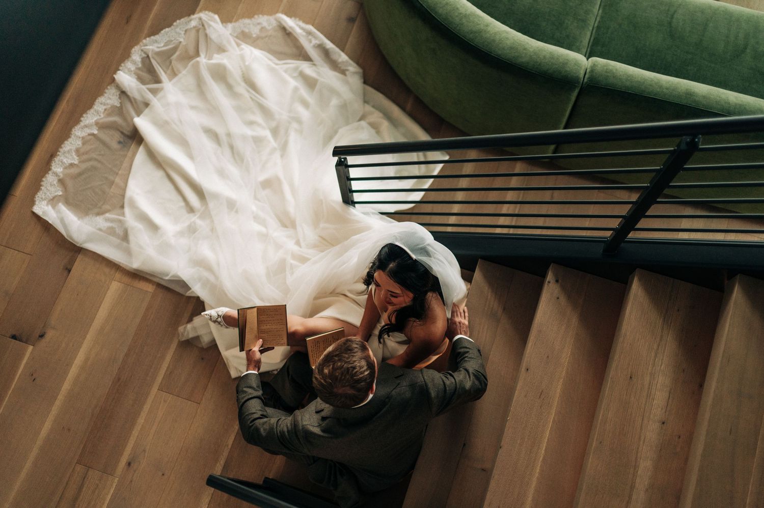 A couple embraces on wooden stairs with flowing white fabric and black railings in an overhead view.