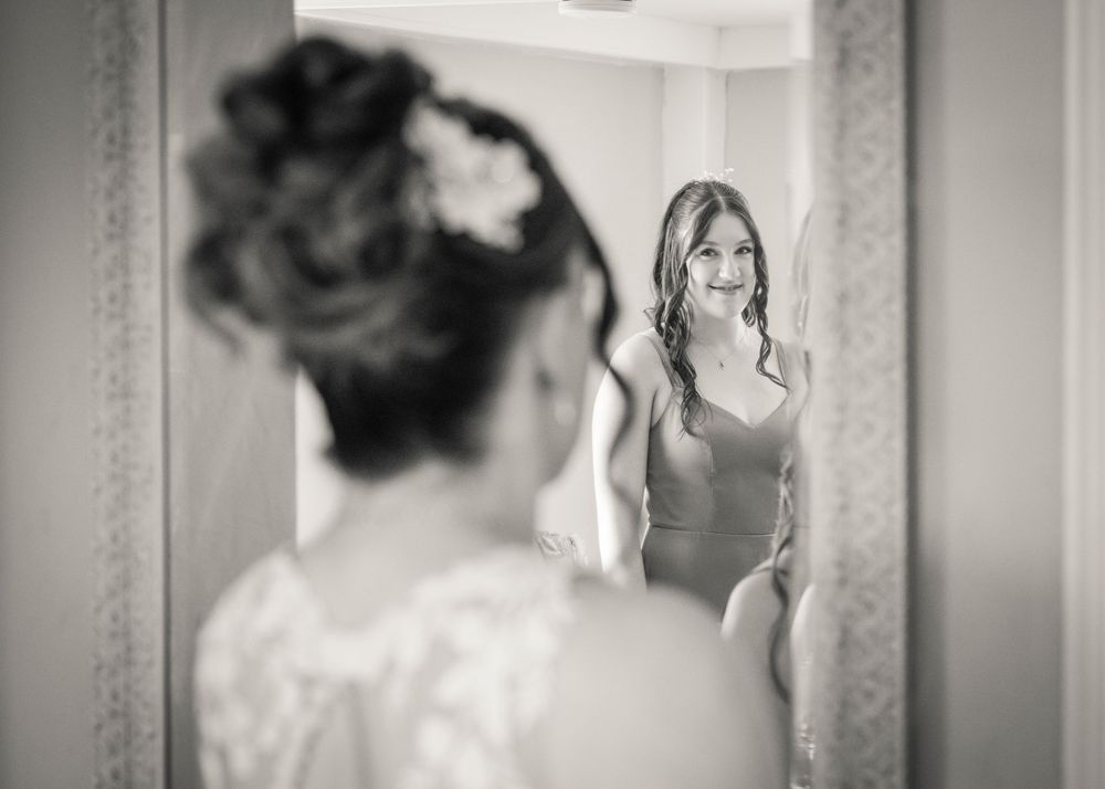 Black and white photo of a smiling bride in wedding dress reflected in a mirror.
