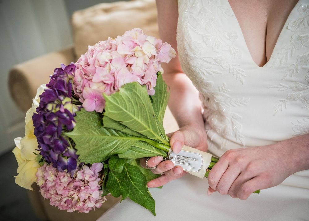 Bride holds a beautiful bouquet of pink and purple hydrangeas with green leaves on her wedding day.