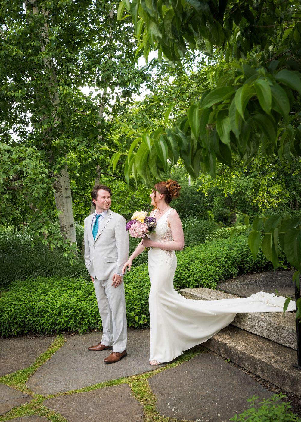 Bride and groom share a romantic first look moment in a lush green garden, bride holding a colorful bouquet.