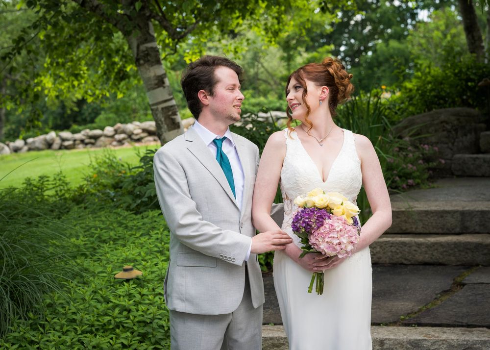 Bride and groom share a joyful moment outdoors, bride holding colorful bouquet in lush garden setting.