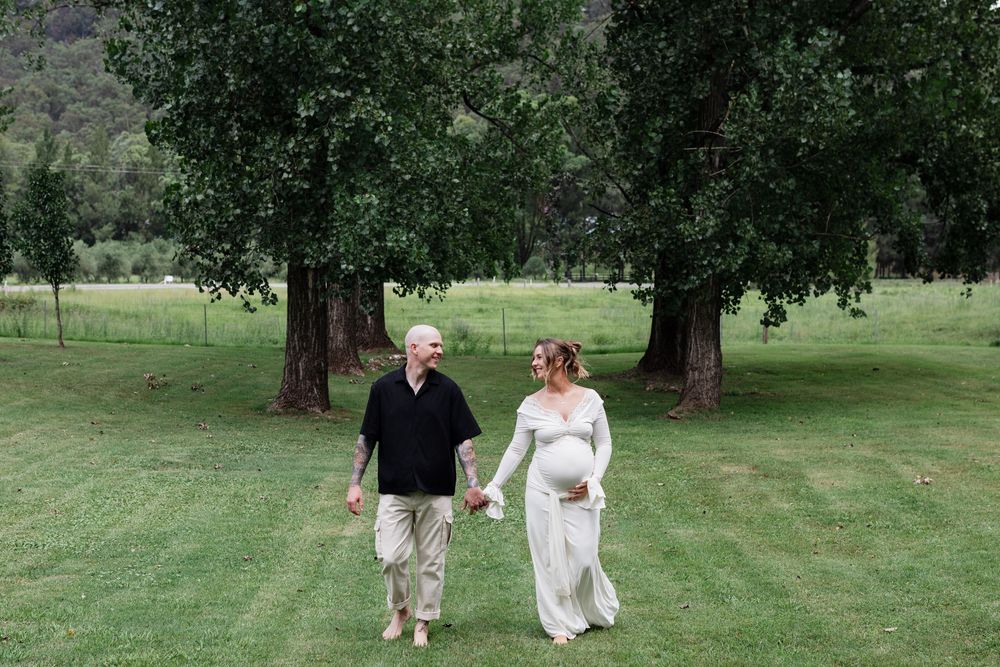 A couple in wedding attire walks hand in hand through a lush green park on their special day.