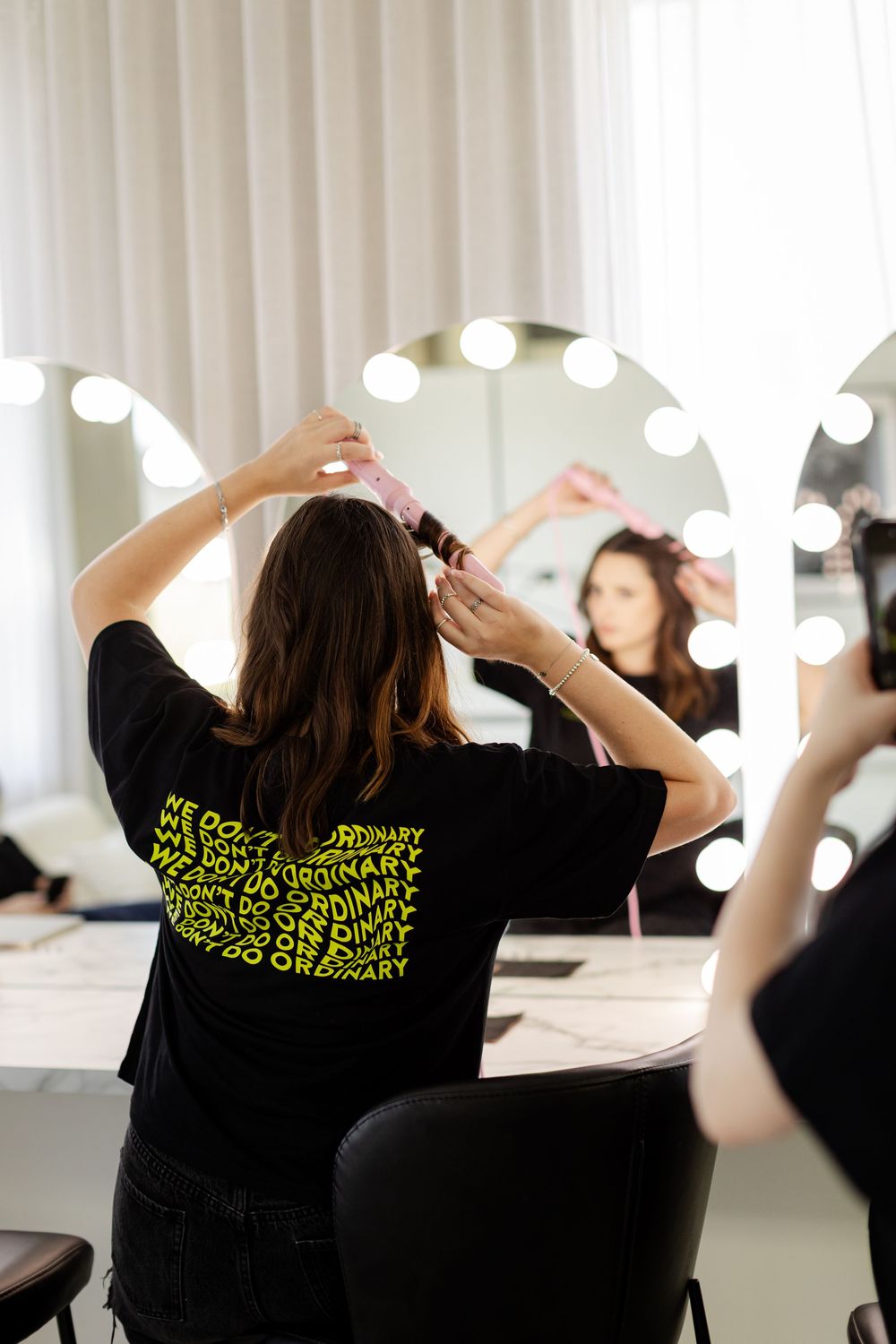 Group of people in black t-shirts with neon text working in a bright studio space with vanity lighting.