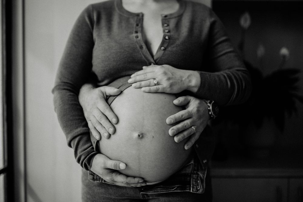 Black and white photograph of hands cradling a pregnant belly in a tender maternity portrait.