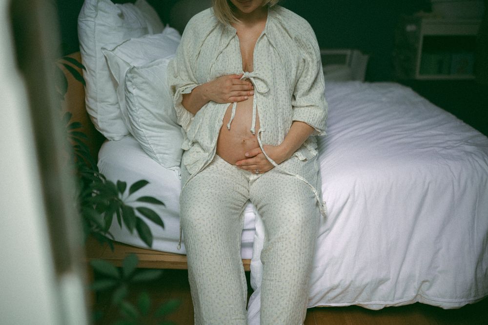 A person in white clothing sits on a bed in a dimly lit room with green-tinted lighting.