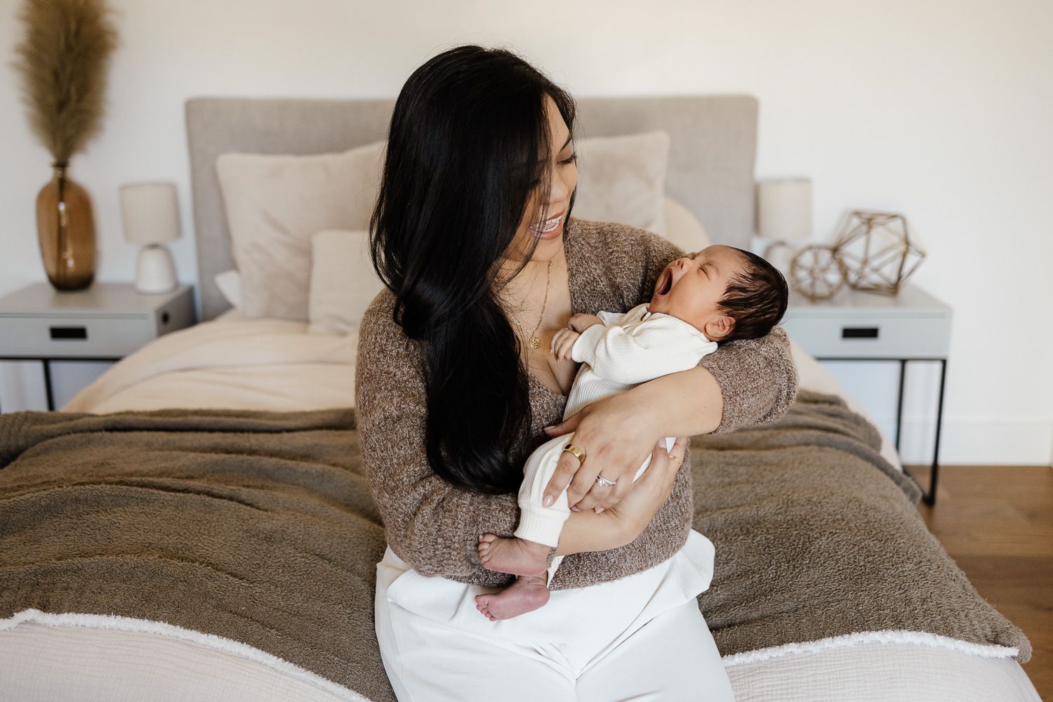 a mom cuddles her baby as he yawns on her bed at her in-home photoshoot with Cindy Tucey Photography
