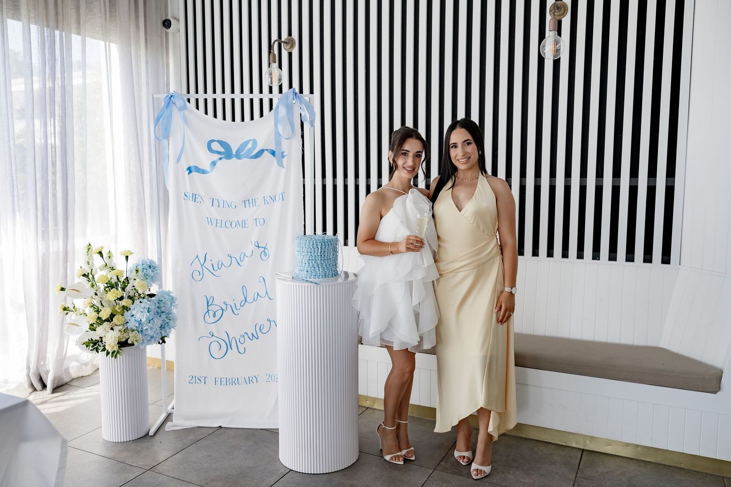 A bridal shower setup with a blue and white theme featuring a decorative sign and white column display.