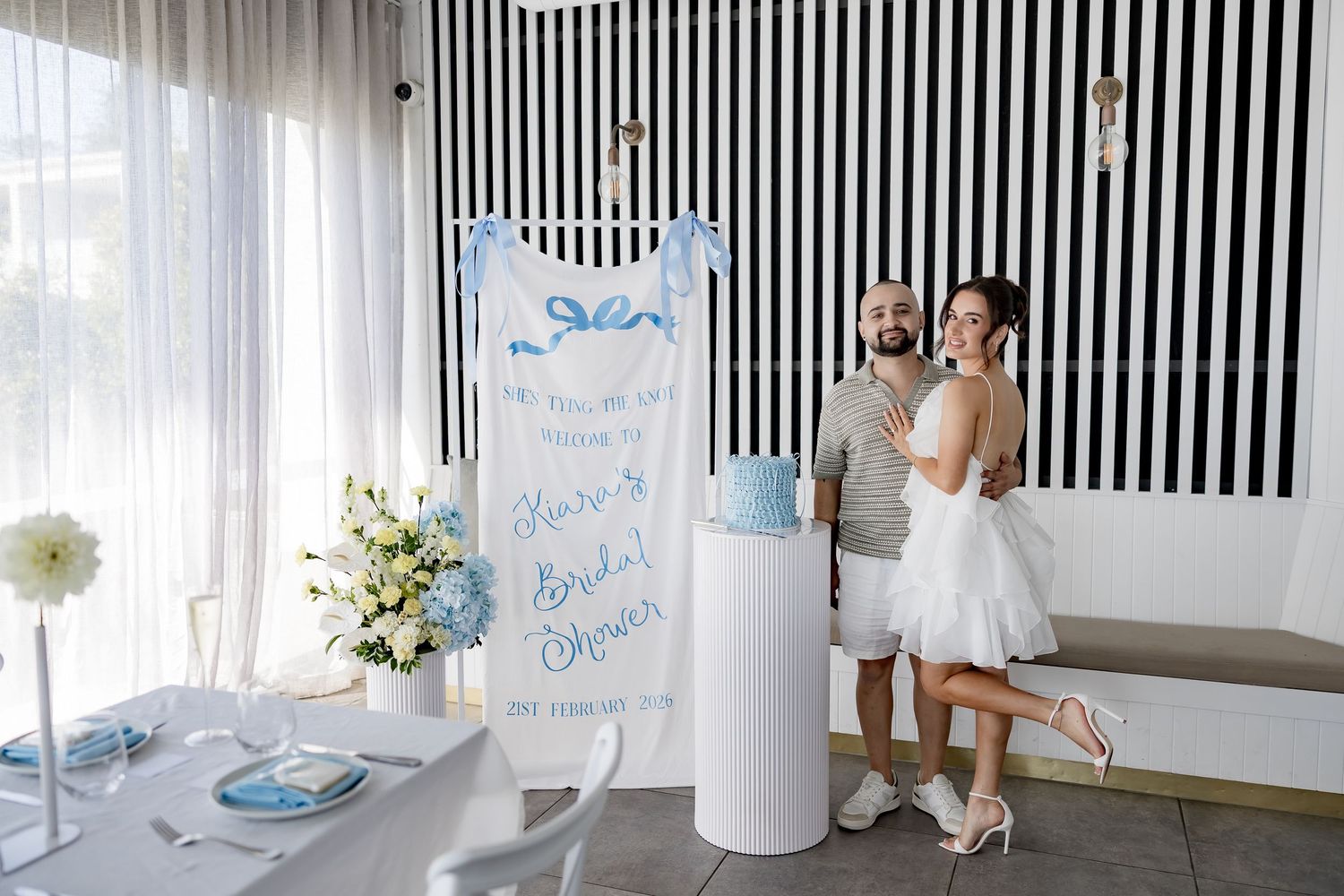 Modern white and blue baby shower celebration setup with striped wall backdrop and elegant party decorations.