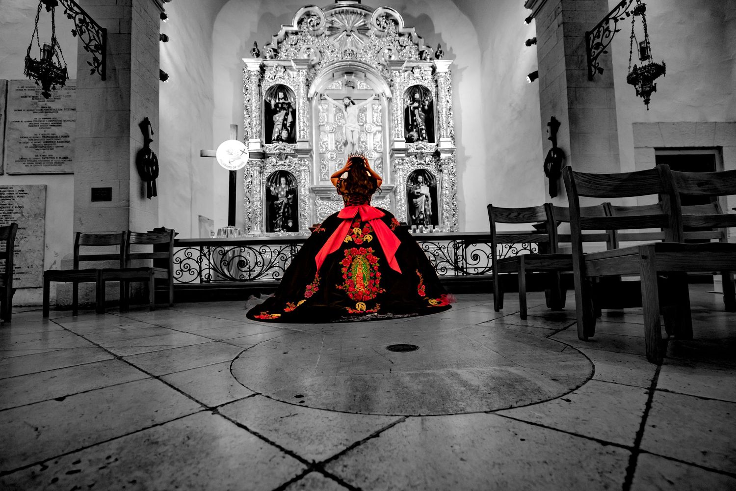 A dramatic red dress stands out in black and white against an ornate church altar with religious statues and decor.