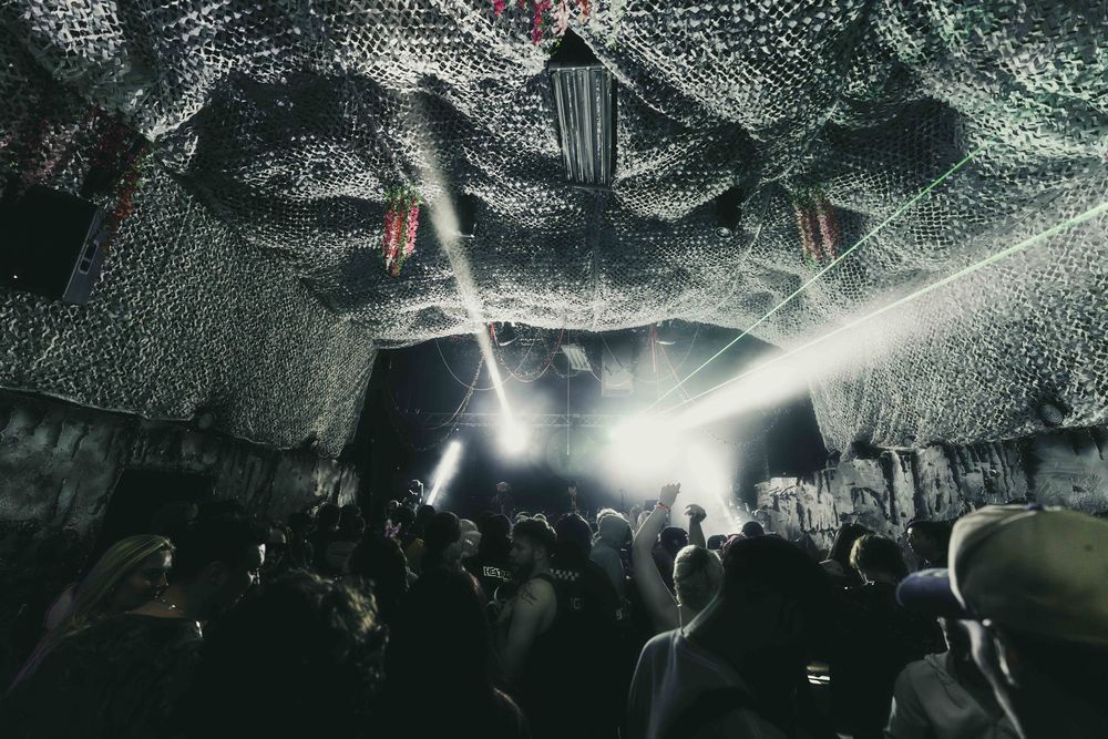 Crowd at an underground nightclub with dramatic lighting and industrial ceiling creating an atmospheric dance environment.