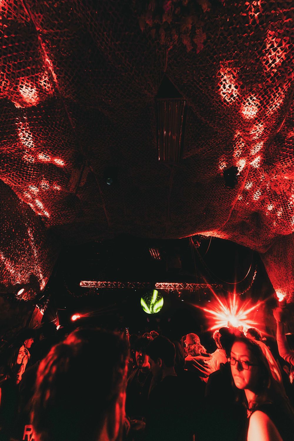 A dark nightclub scene illuminated by red lights with silhouettes of people dancing under atmospheric lighting.