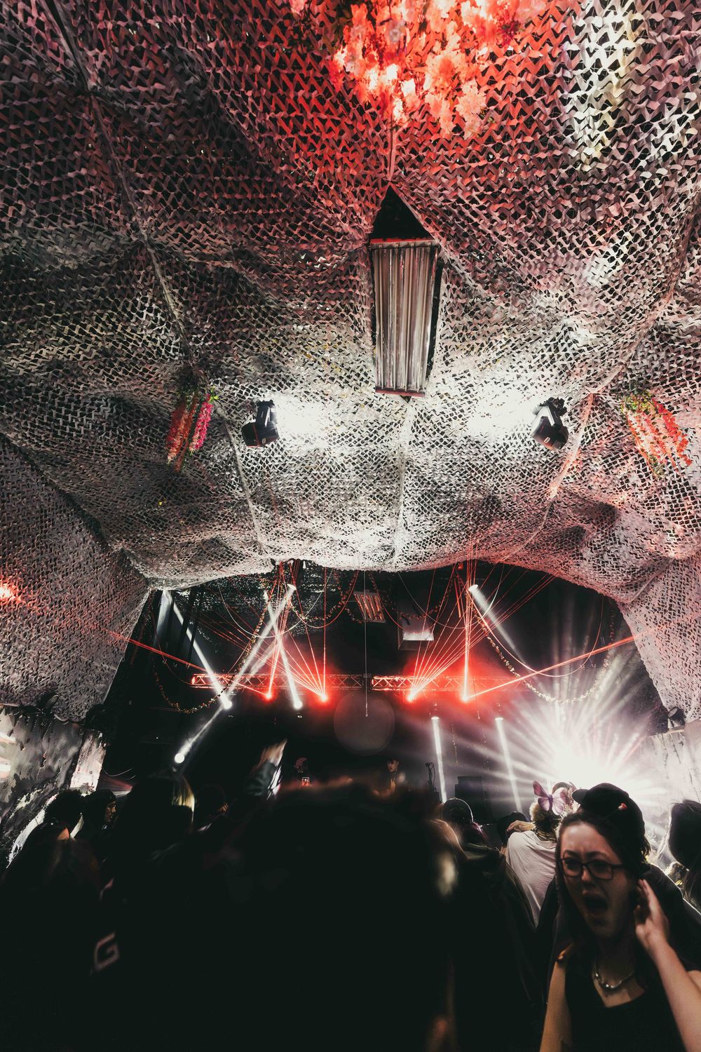 Concert crowd silhouettes under dramatic red and white mesh lighting effects creating an immersive atmosphere at night.