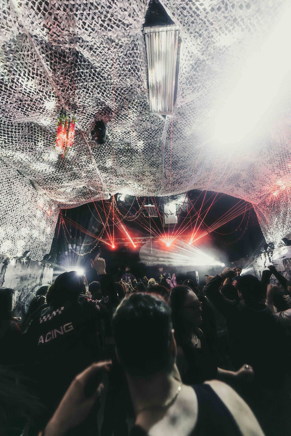 Disco ball reflects light over a crowded nightclub dance floor with red lighting effects and silhouetted party crowd.