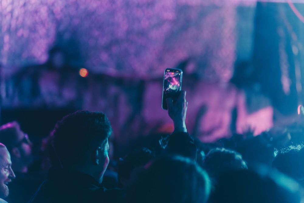 Concert crowd silhouettes against vibrant purple stage lighting at a live music performance.
