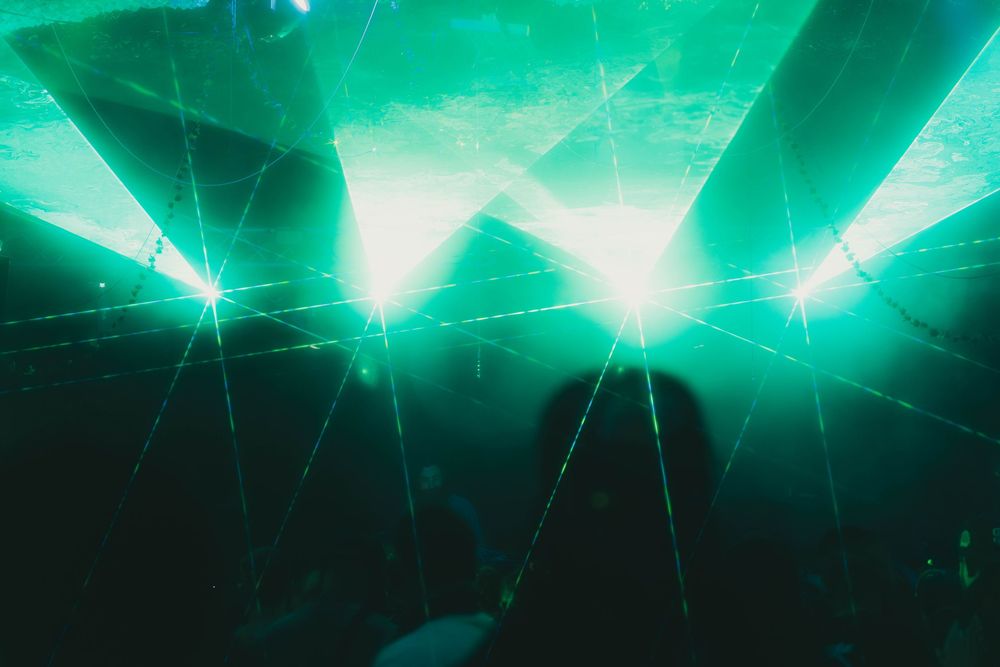 Bright green laser lights shine through smoke at a concert or nightclub creating dramatic geometric patterns.