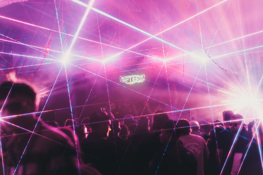 Silhouetted crowd at a nightclub with pink lighting and crisscrossing laser beams creating a dynamic atmosphere.