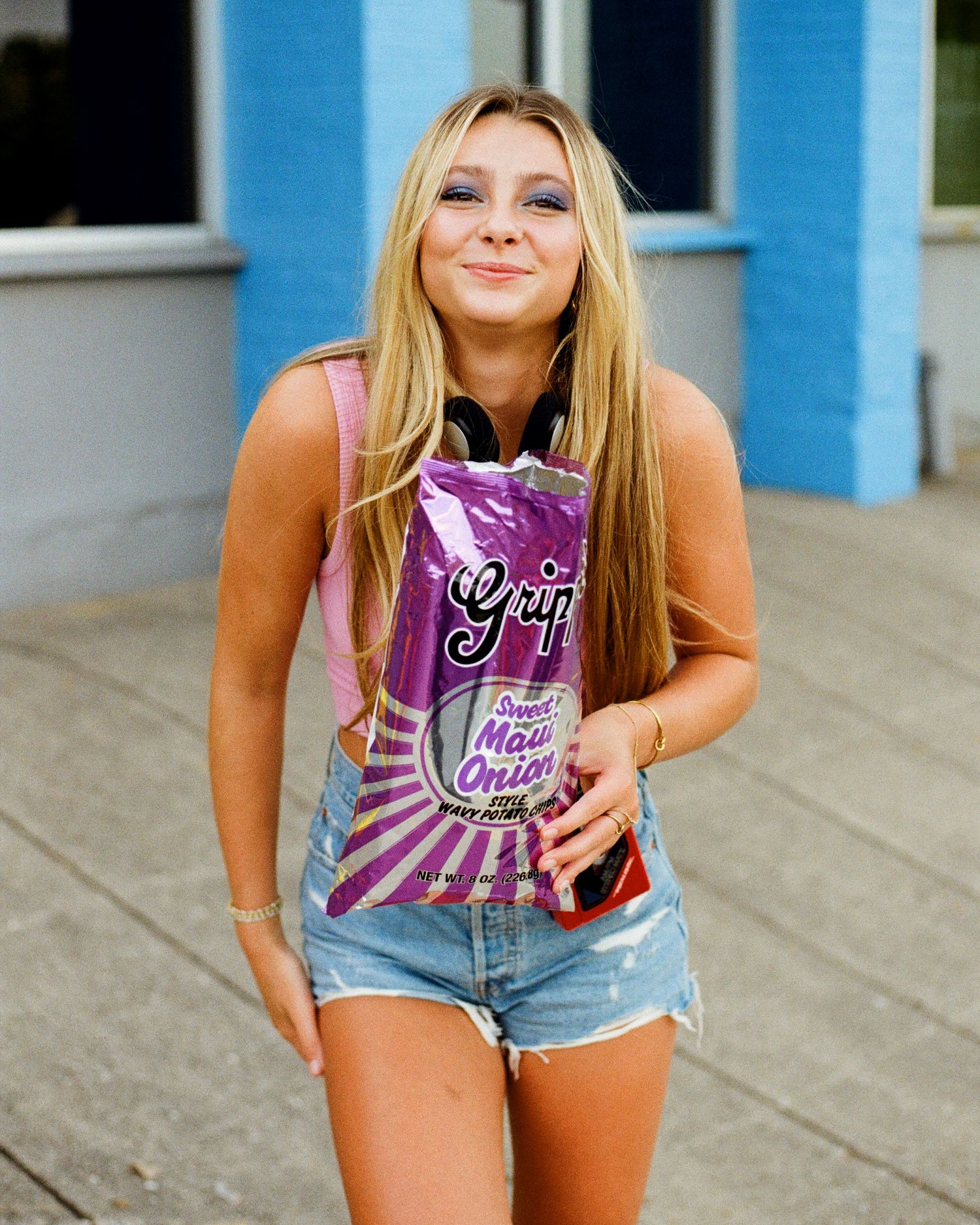A series of photos showing someone in denim shorts and a hot pink tank top holding a purple foil bag of potato chips.