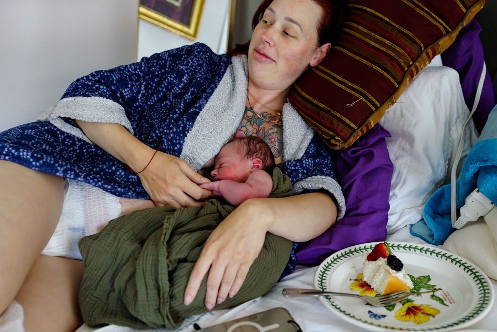 A person rests their head on a table next to a plate with a partially eaten meal.