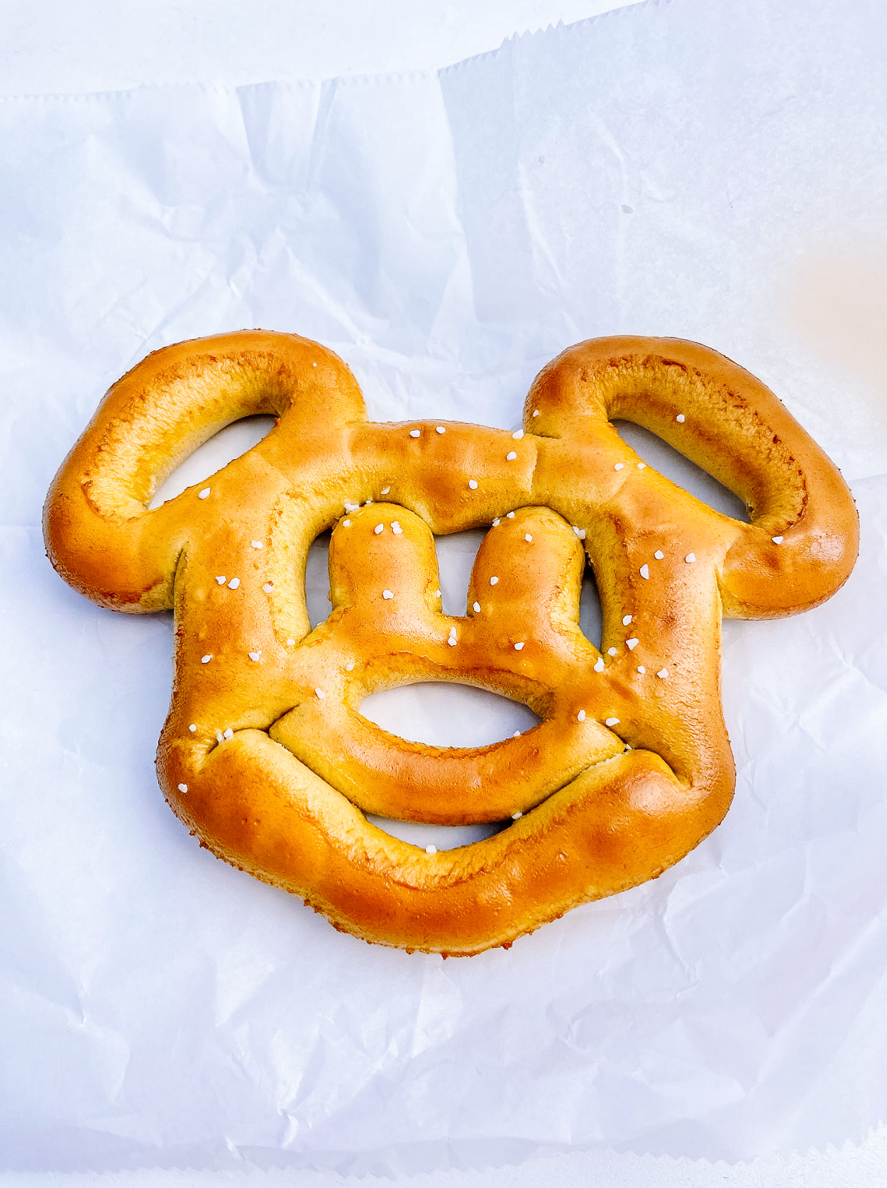 A golden-brown Mickey Mouse shaped pretzel with salt on white paper background.