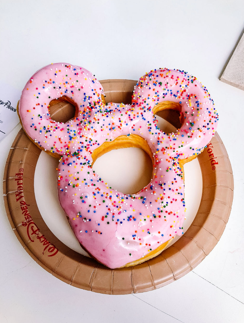 Pink frosted Mickey Mouse shaped donuts with colorful sprinkles arranged in stop motion sequence on wooden plates.