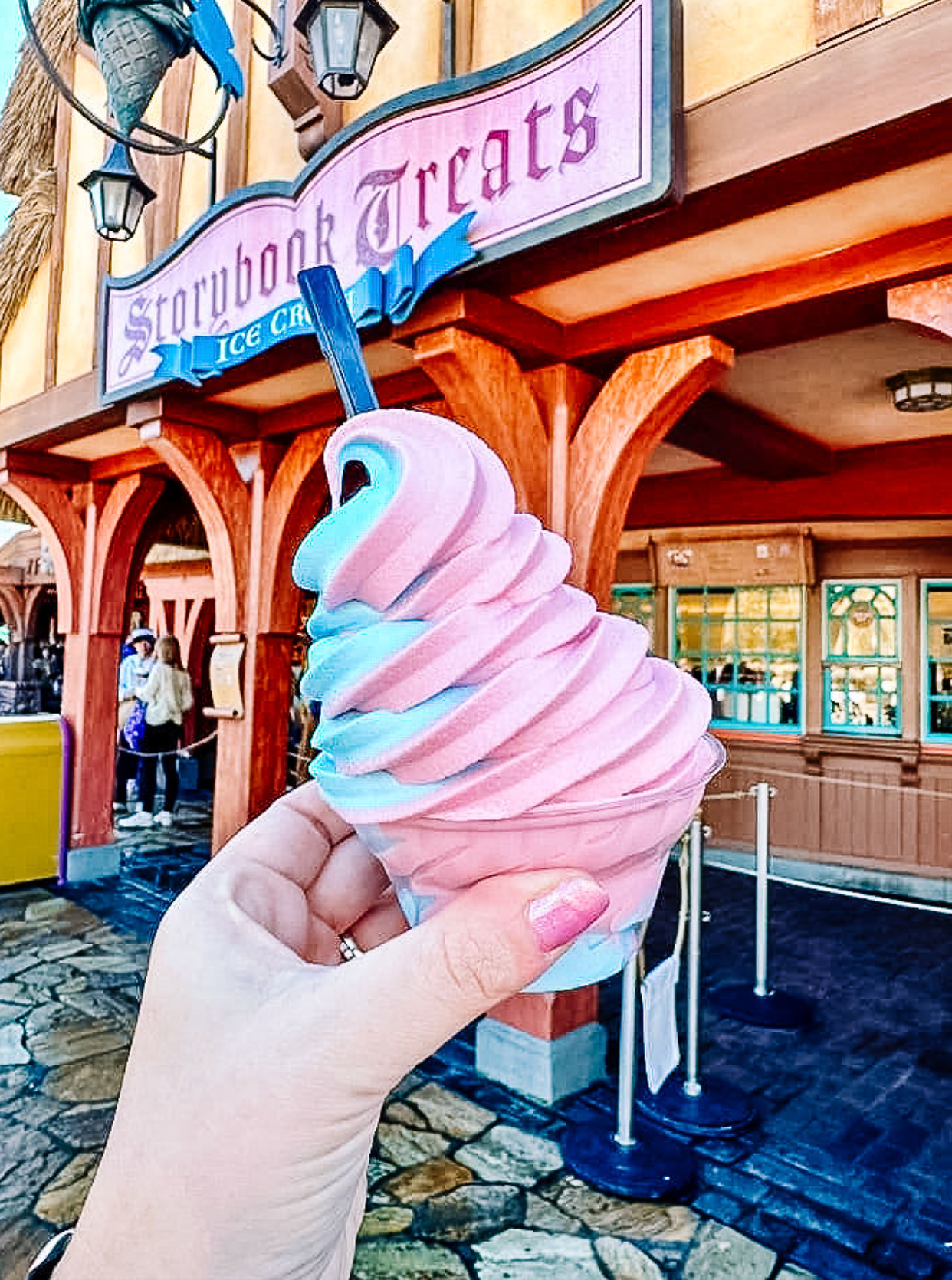 A pink cotton candy flavored Dole Whip swirl served in a white paper cup against an outdoor theme park setting.