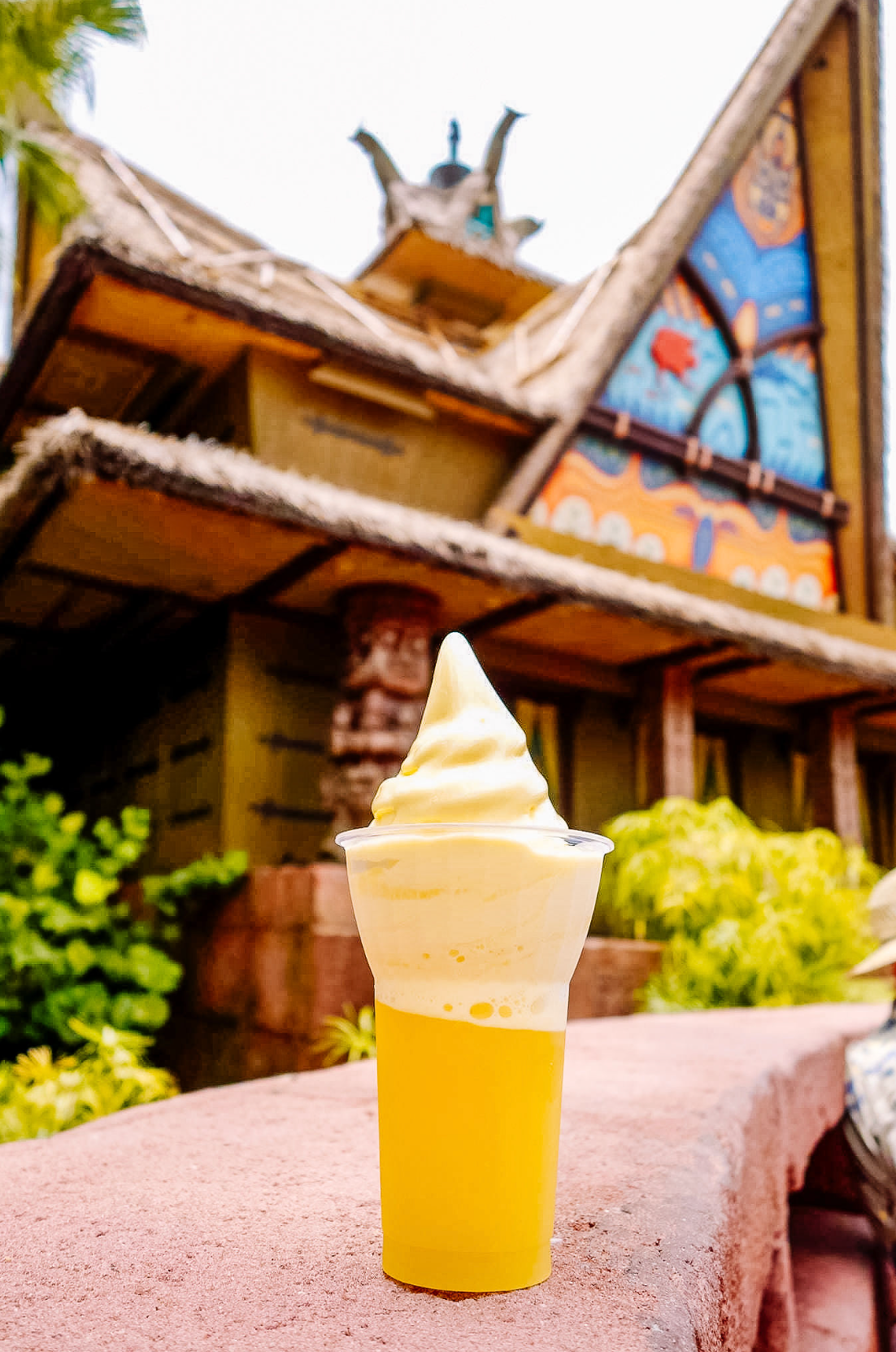 Three identical servings of Dole Whip soft serve ice cream in yellow cups sit on a stone ledge at Disney theme park.