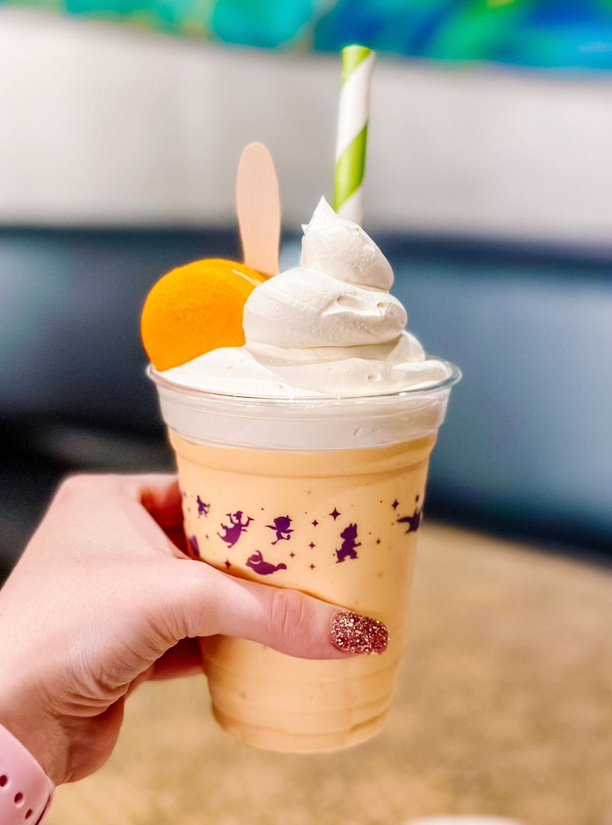 Orange creamsicle smoothie topped with whipped cream and a straw in a plastic cup decorated with purple flowers.
