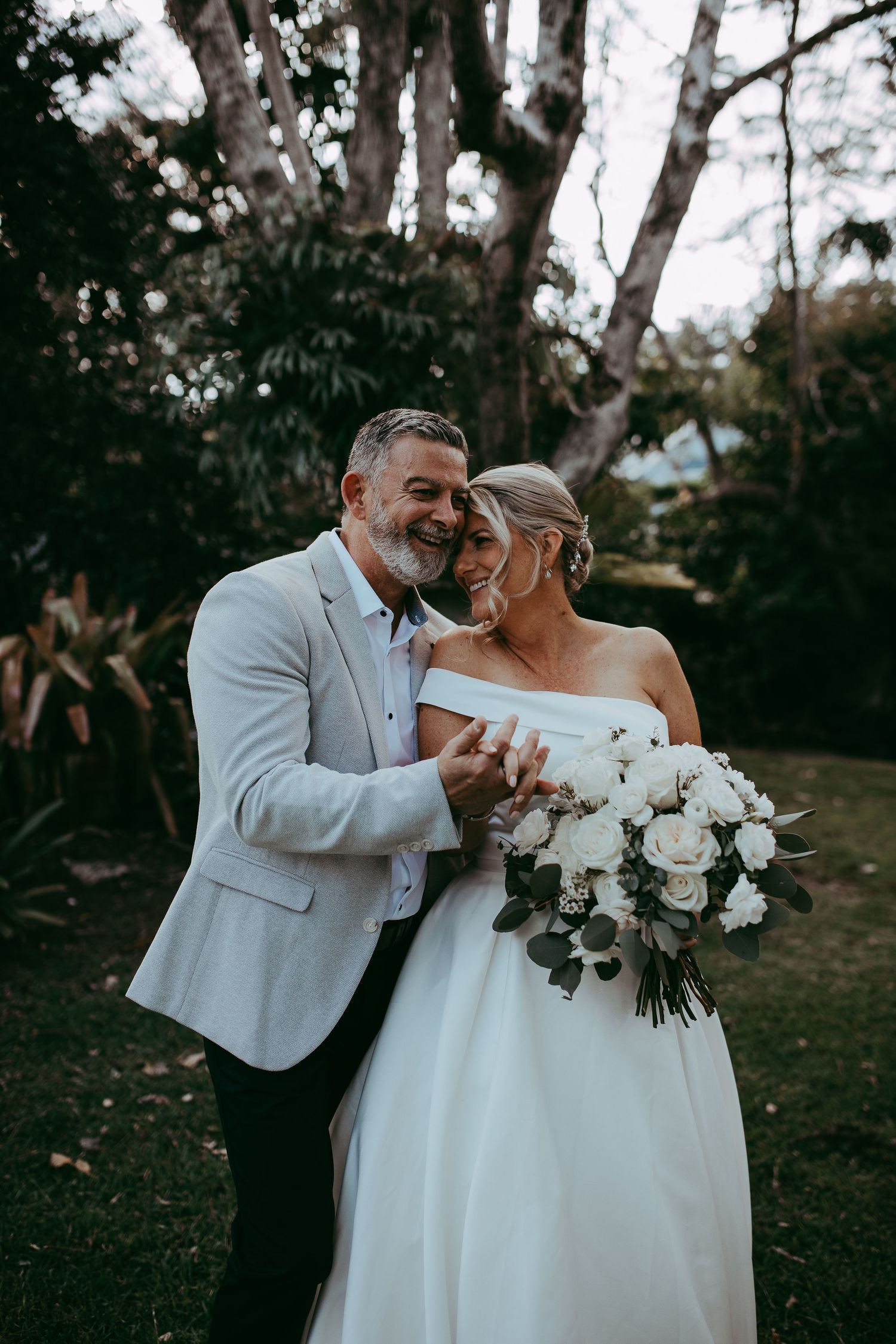 A couple shares a joyful moment at their outdoor wedding, with the bride holding a white rose bouquet.