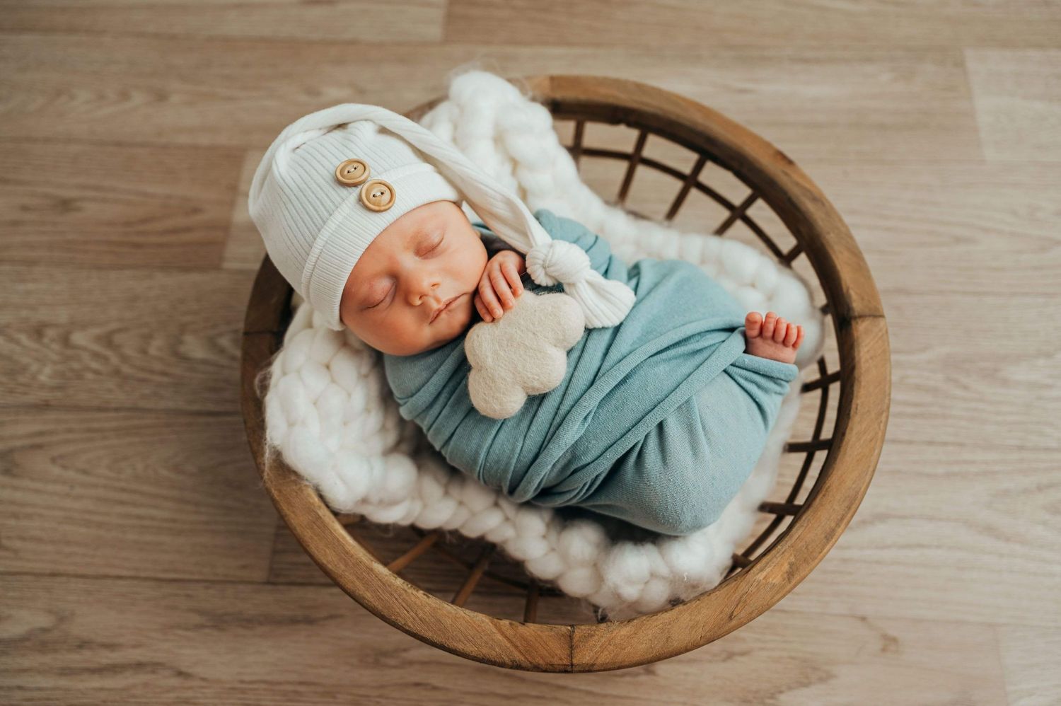 Sleeping newborn baby wrapped in blue swaddle lying in round wooden basket. rockford il family newborn photographer