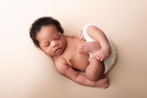 Peaceful sleeping newborn baby in white diaper lying on beige backdrop during professional photoshoot.