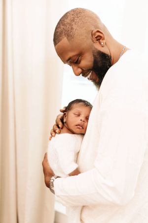 A tender moment between a parent and sleeping baby, both wearing white against a light background. Dallas newborn photographer that provides