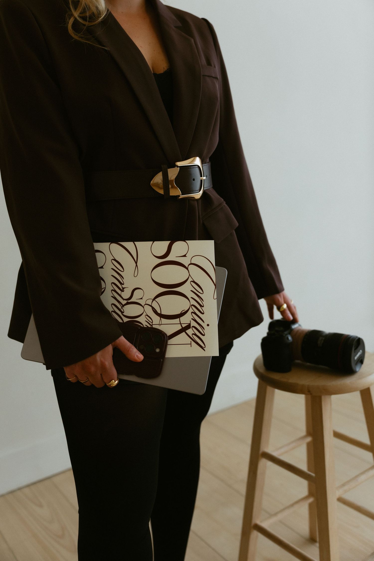 Woman in gray blazer and black outfit poses against white studio backdrop.