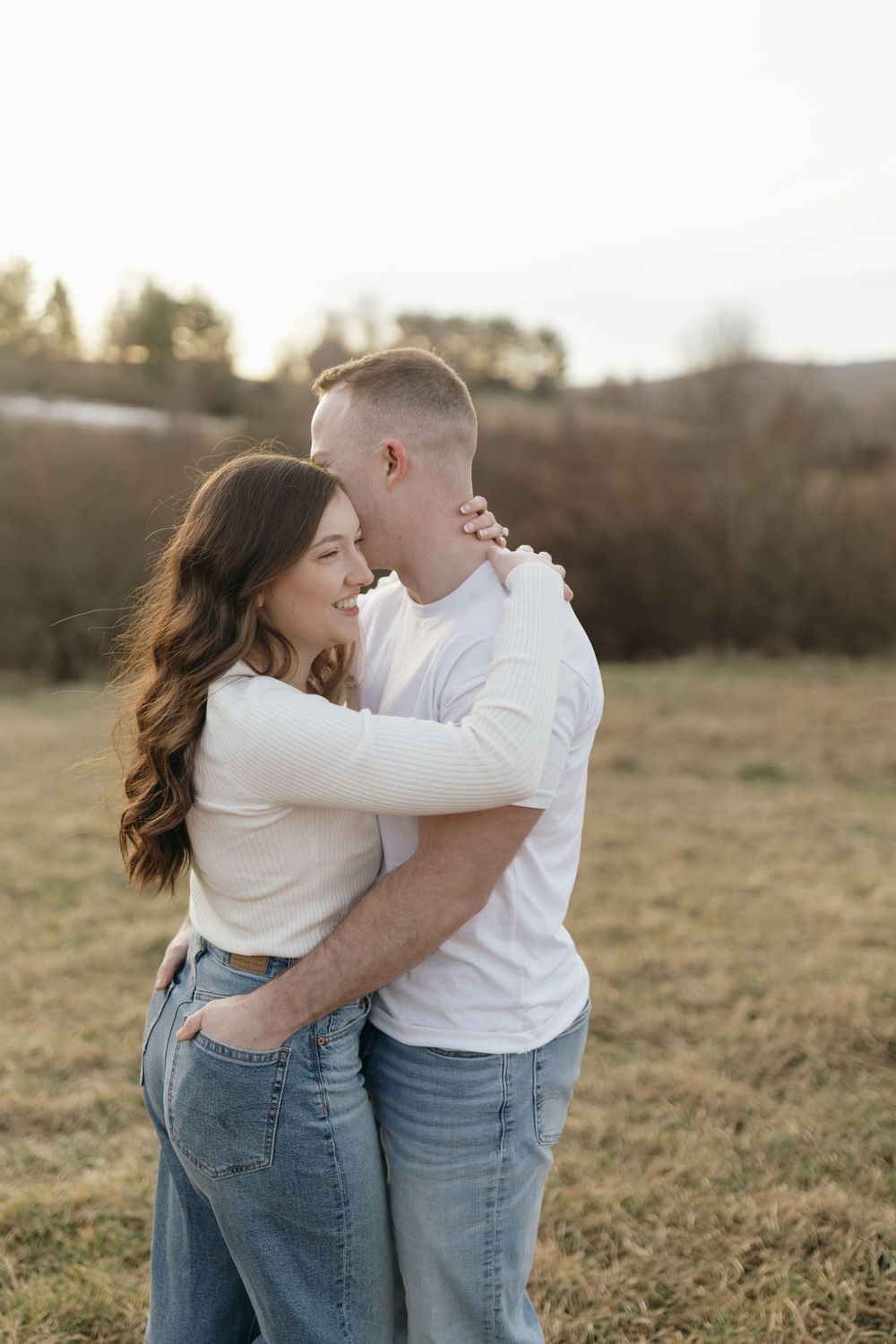 Couple embracing tenderly in casual outfits during outdoor sunset photoshoot.