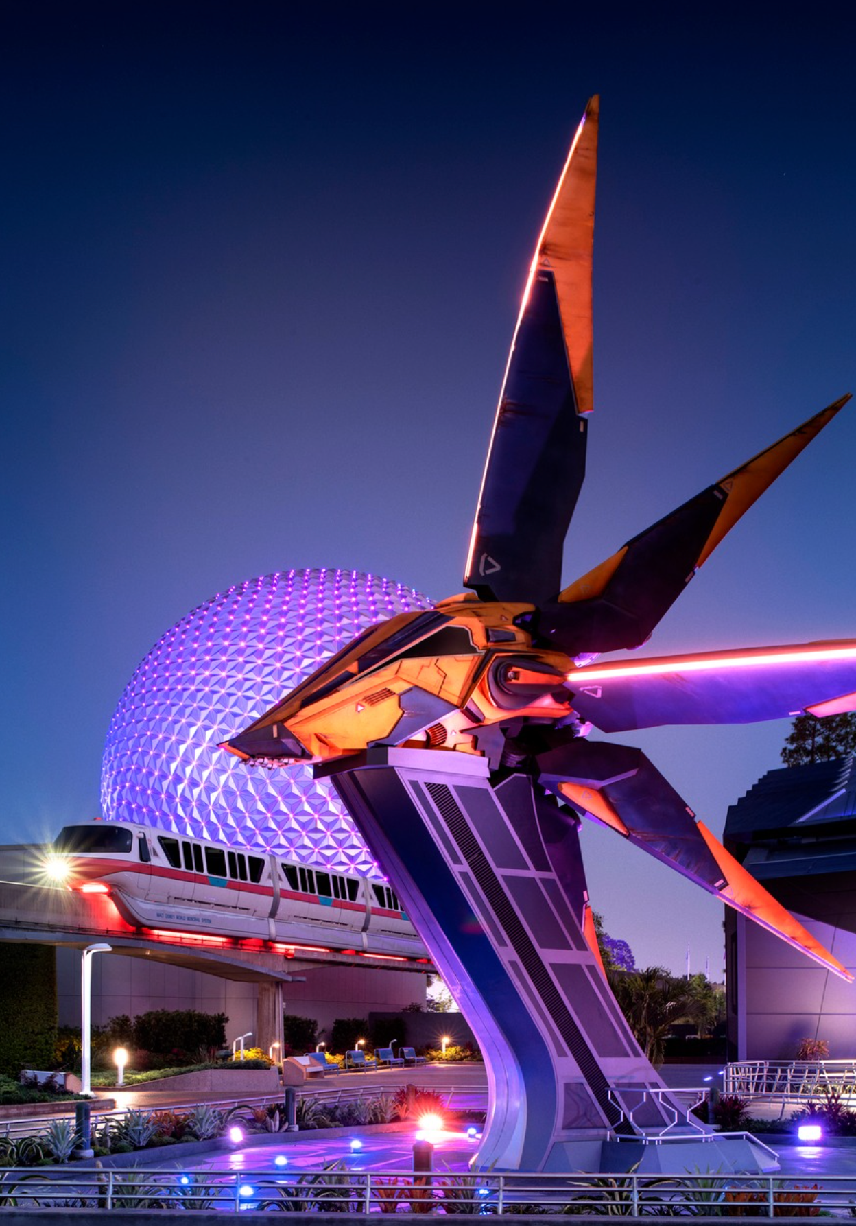 Illuminated monorail track and futuristic sculpture at Epcot's Mission Space pavilion with purple lighting at dusk.