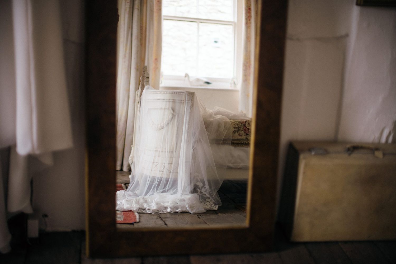 Mirror reflection showing a vintage bedroom interior with a white bridal veil draped over a bed near a window at Healy Events, Kentville