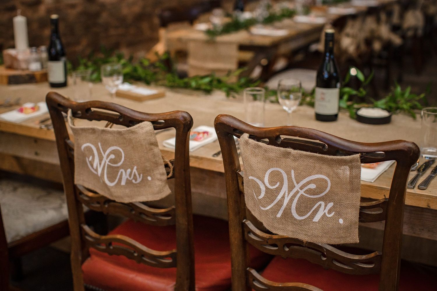 Rustic wooden chairs with Mr and Mrs signs at a vintage wedding reception table setting decorated with wine bottles at Healy Events, NS