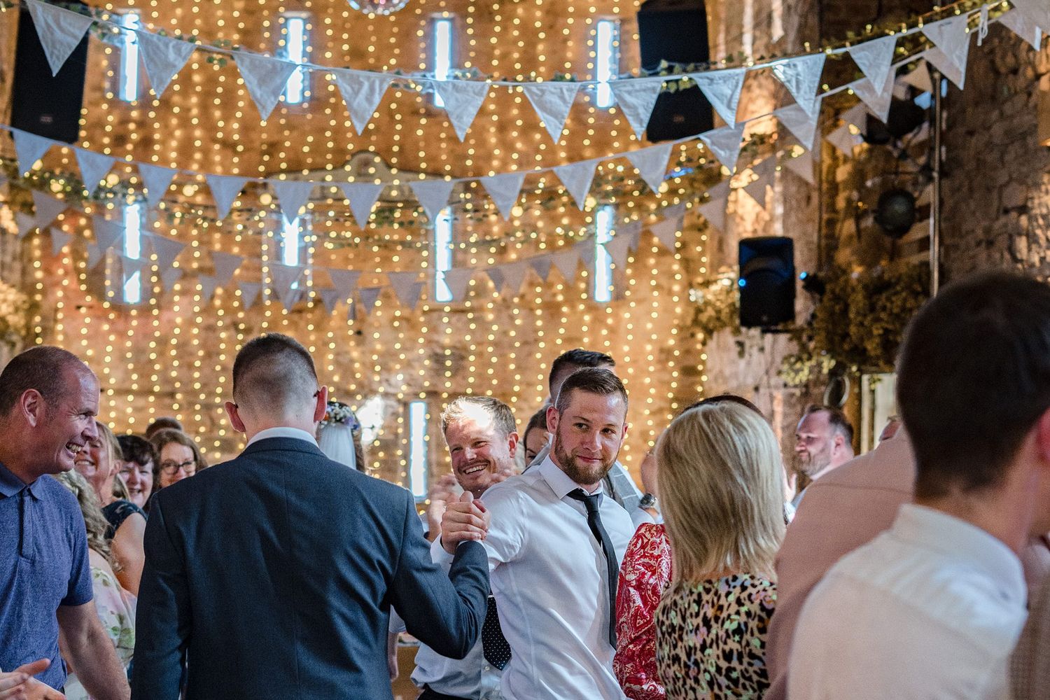 Wedding guests celebrate under warm twinkling string lights hanging in a rustic Healy Events stone venue during a reception.