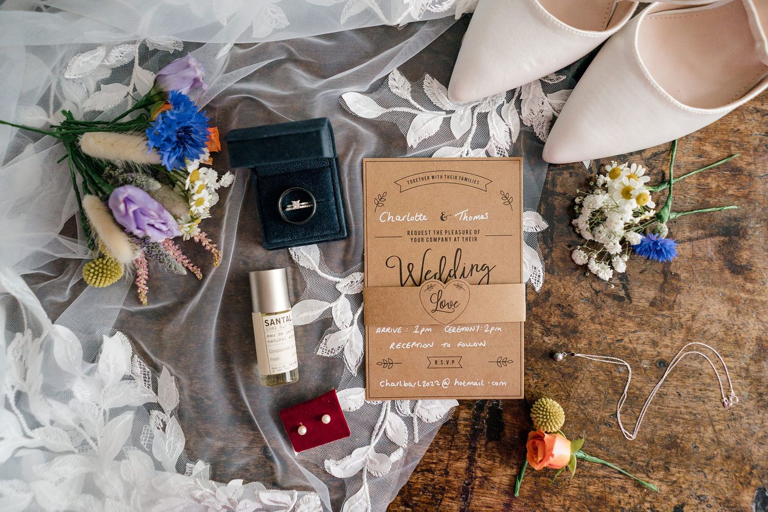 Wedding details including a wooden invitation, flowers, rings, and accessories arranged on a rustic surface at Healy Events wedding venue