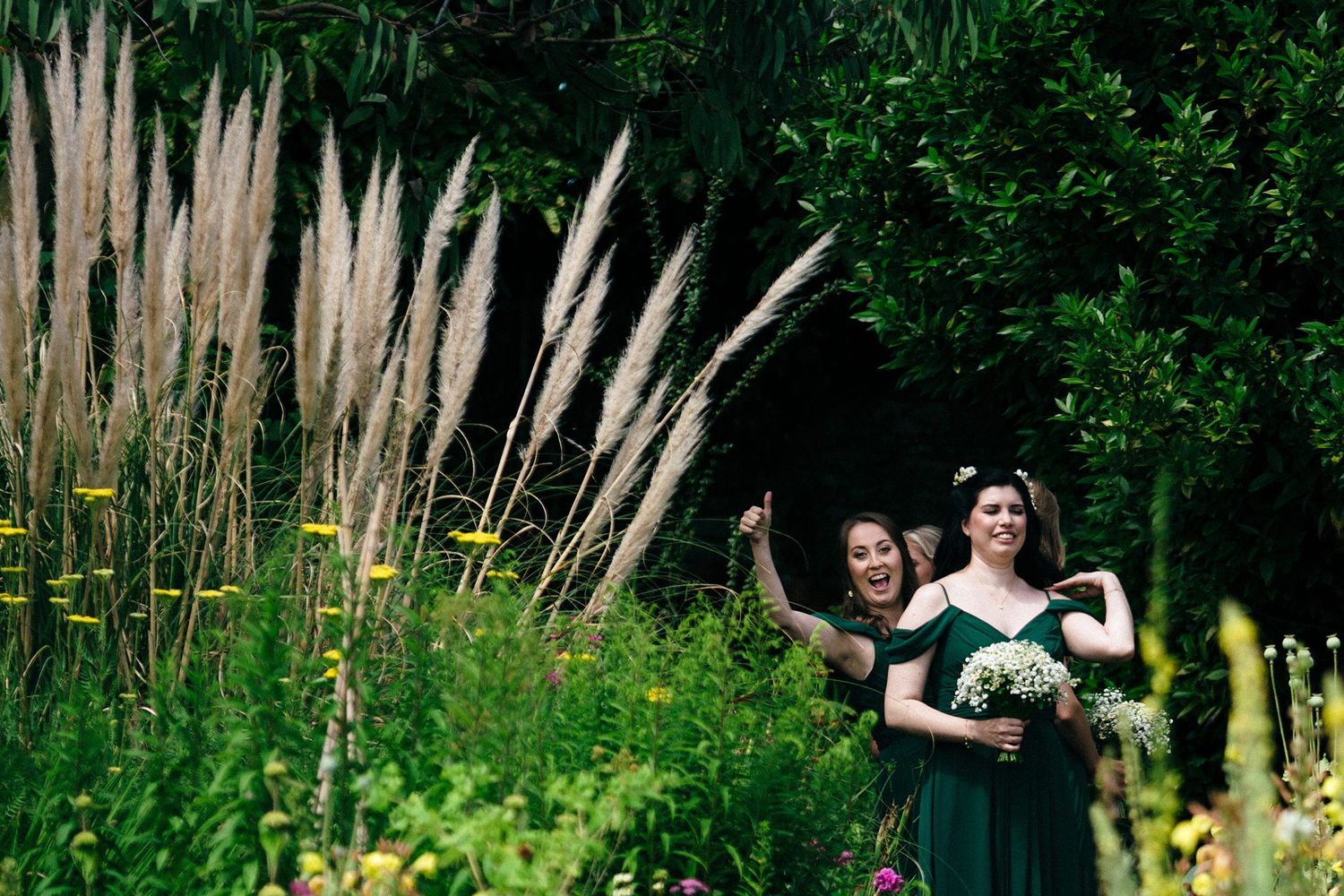 Two bridesmaids walk amid tall ornamental grasses and lush greenery in a natural garden setting at Healy Events wedding venue.