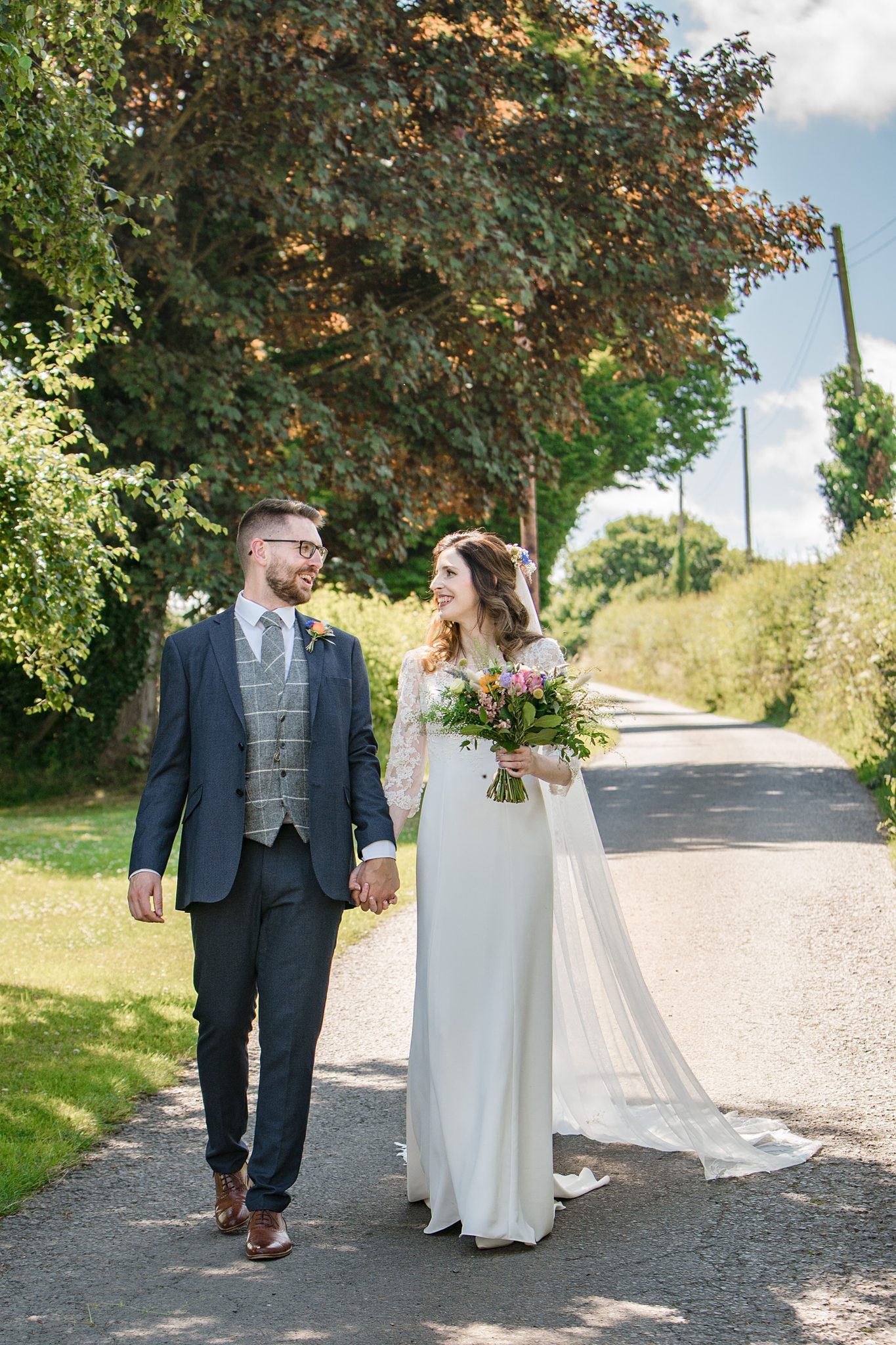 A couple walks down a countryside path together on their wedding day in summer near Healy Events, Kentville, Nova Scotia with photographer